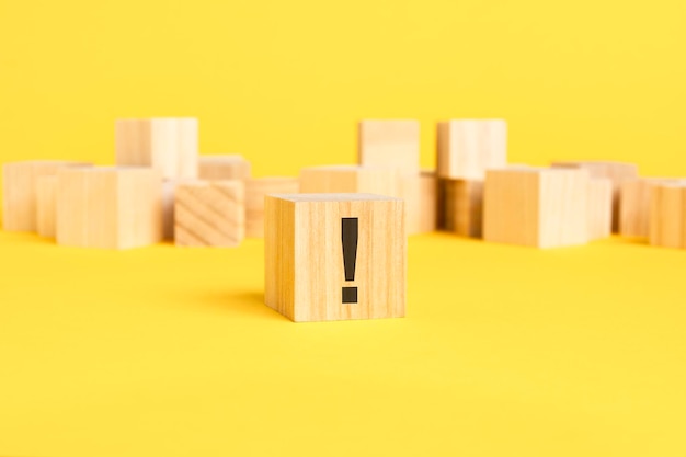 Wooden block with exclamation mark sign on a wooden block on a yellow background with copy space black symbol