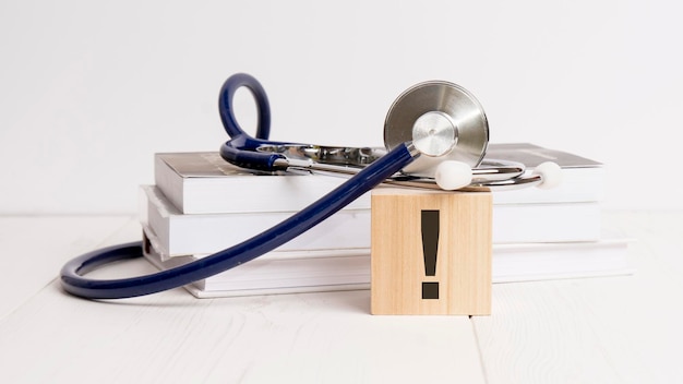 Wooden block with exclamation point stethoscope book notepad on white wooden table medical and education concept