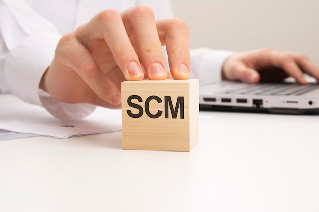 A wooden block with the letters SCM written on it on a white background SCM short for Supply Chain Management