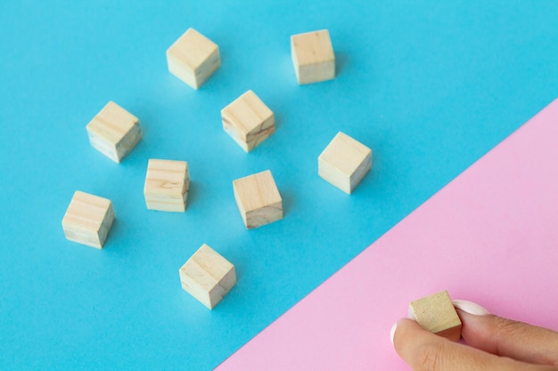 Wooden blocks with a human hand placing one cube at the top on blue background