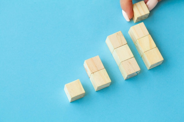 Wooden blocks with a human hand placing one cube at the top on blue background