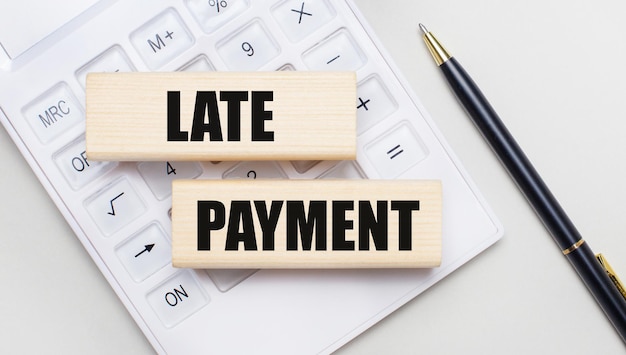 Wooden blocks with the LATE PAYMENT lie on a light background on a white calculator. Nearby is a black handle. Business concept