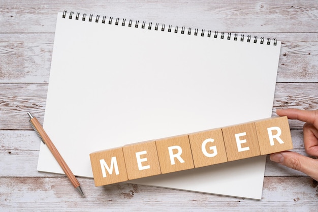 Wooden blocks with MERGER text of concept, a pen, and a notebook.