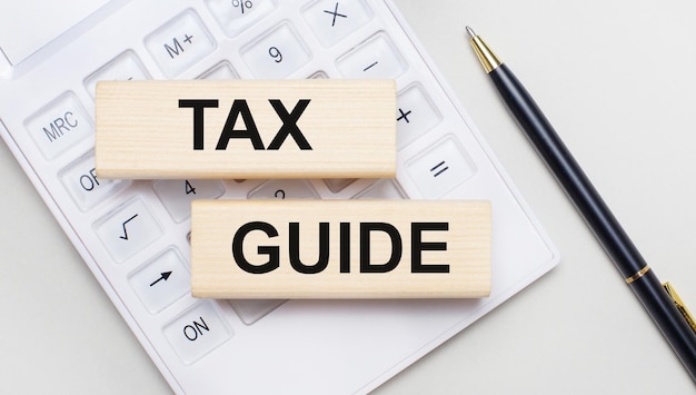 Wooden blocks with the TAX GUIDE Iie on a light background on a white calculator Nearby is a black handle Business concept