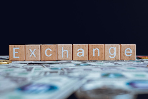 Photo wooden blocks with the text exchange on a black background and crypto banknotes scattered on the g