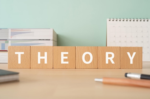 Photo wooden blocks with theory text of concept, pens, notebooks, and books.