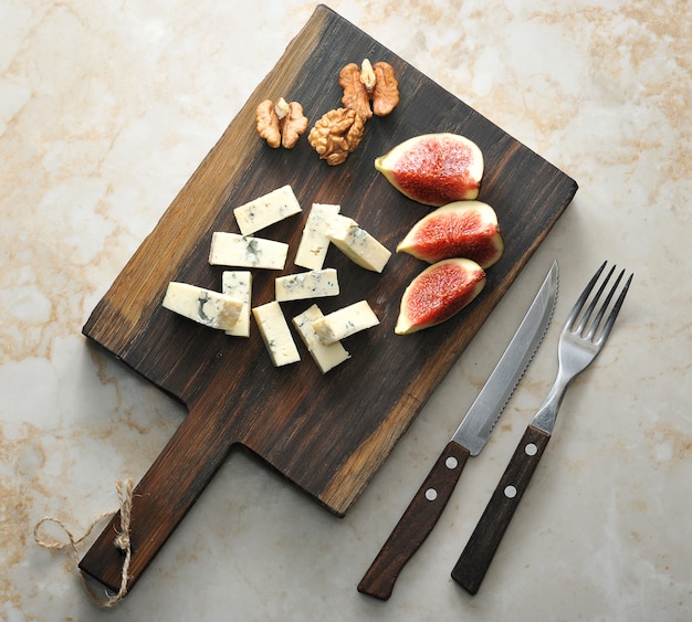 On a wooden board, cheese with blue mold dorblu, a few figs and walnuts.