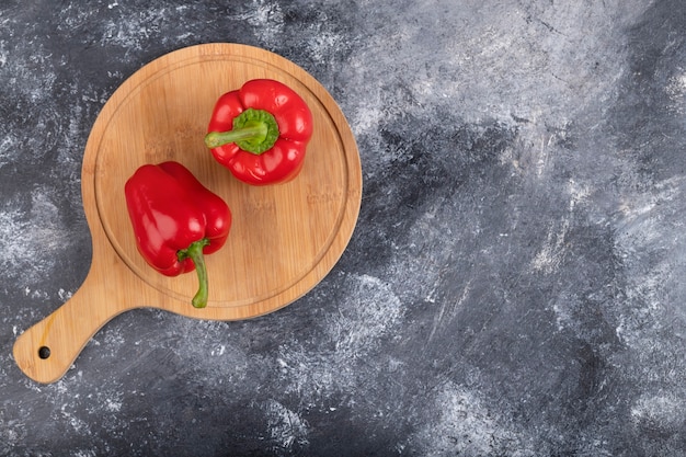 Wooden board of red bell peppers on marble surface.