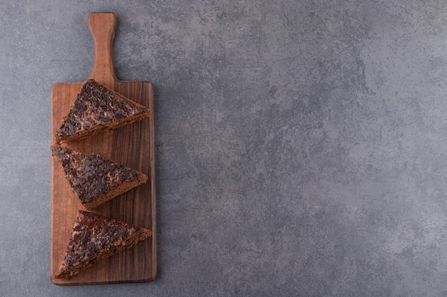 Wooden board of sweet sliced cake on stone table.