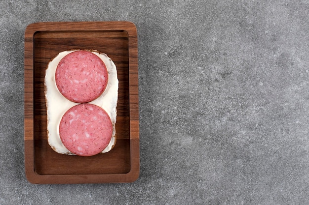 Wooden board of toast with salami placed on stone.