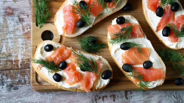 A wooden board with bread, smoked salmon and black olives on it