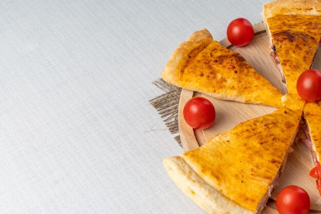 A wooden board with pizzas on it and tomatoes on the side