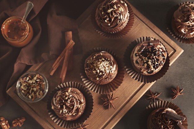 Photo wooden board with tasty chocolate cupcakes on table