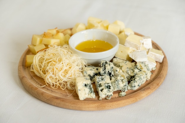 Wooden board with various types of cheeses and bowl of honey, healthy snack, selective focus