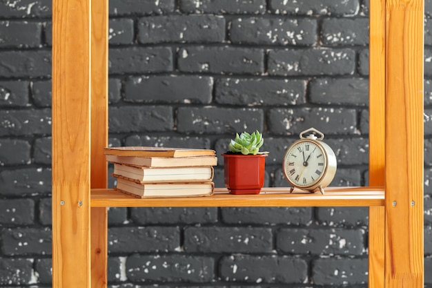 Photo wooden bookshelf with books and stuff against black brick wall