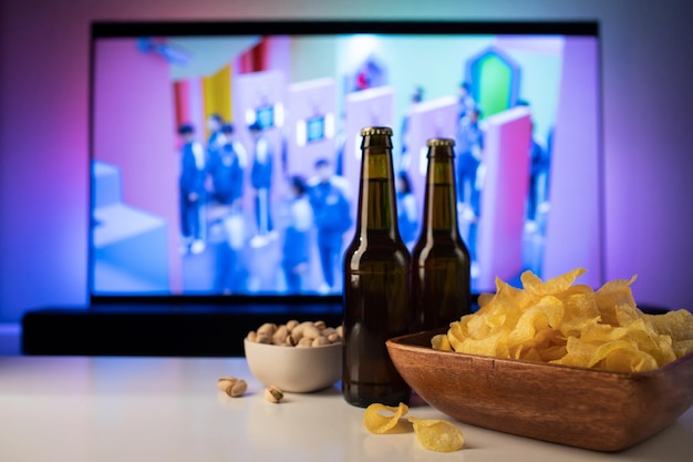 A wooden bowl of chips and snacks in the background the TV works. Evening cozy watching a movie or TV series at home with glass of beer.