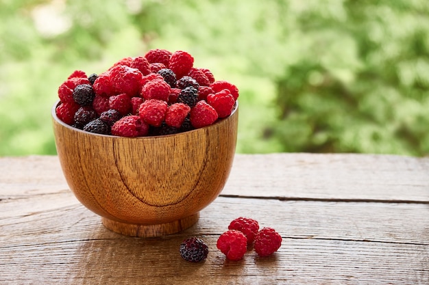 Wooden bowl of delicious red and black raspberries on a background of green foliage