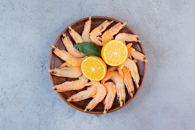 A wooden bowl of delicious shrimps with sliced lemon on a stone background .