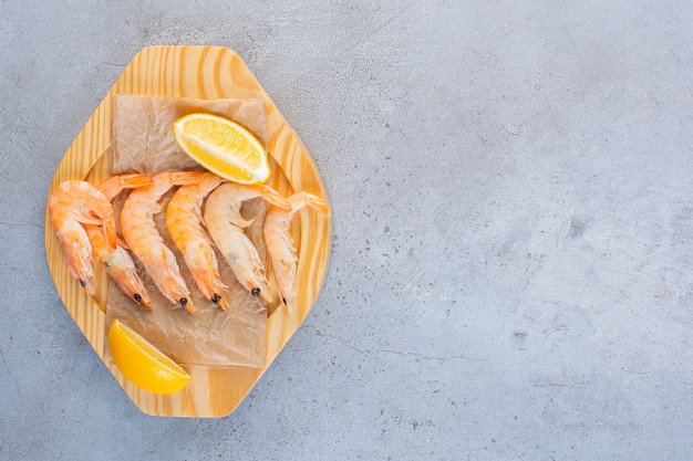 A wooden bowl of delicious shrimps with sliced lemon on a stone surface 