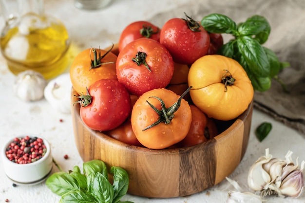 Wooden bowl of fresh colorful tomatoes garlic basil pepper and olive oil on textured background