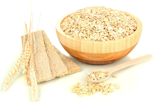 Wooden bowl full of oat flakes with wooden spoon spikelets and oat biscuits isolated on white