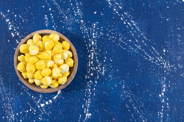 Wooden bowl full of yellow hard candies on blue.