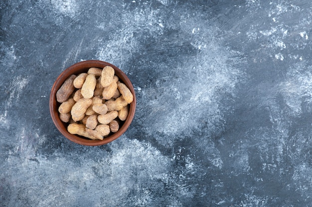 Wooden bowl of organic shelled peanuts on marble table.