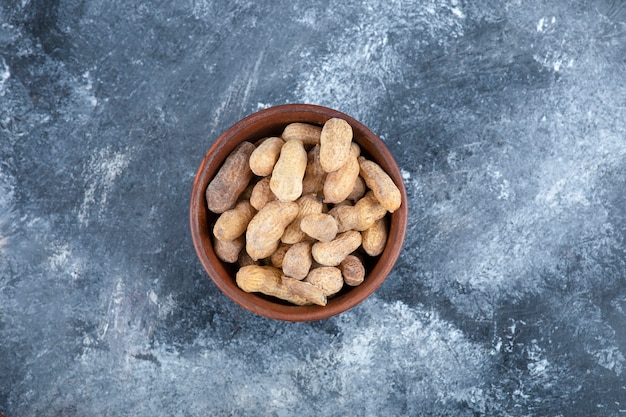 Wooden bowl of organic shelled peanuts on marble table.