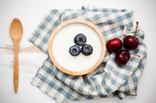 wooden bowl of plain yoghurt with fresh cherry and blueberry.