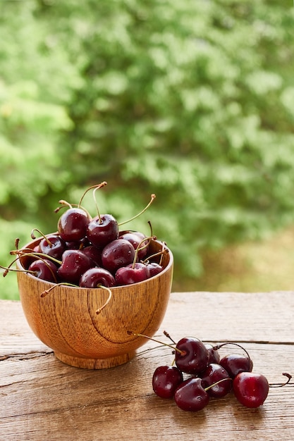 Wooden bowl of ripe, tasty, red cherries on a rustic wooden table on a green natural background, vertical image