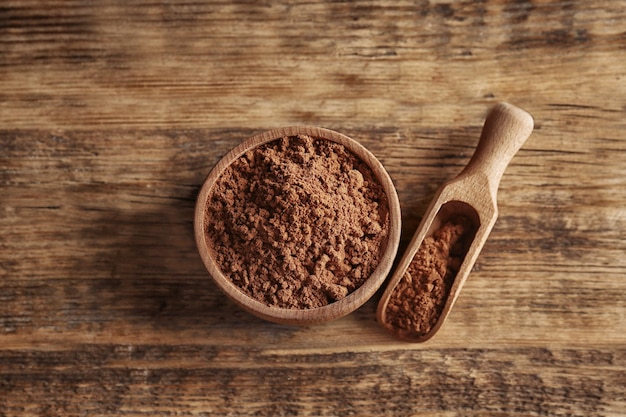 Wooden bowl and scoop with cocoa powder on rustic background