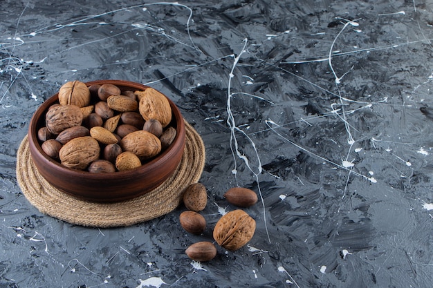 Wooden bowl of shelled various nuts on marble surface.