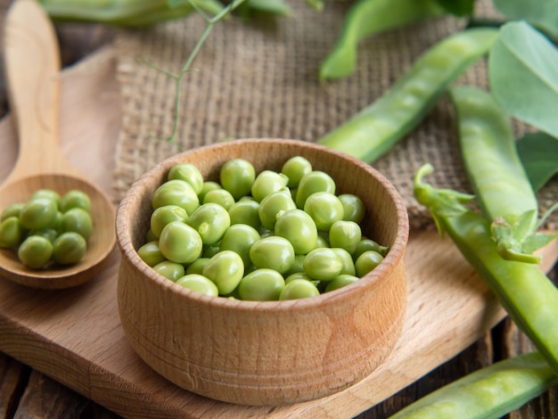 Wooden bowl and spoon with fresh peas and their pods on an old wooden table rustic background with peas