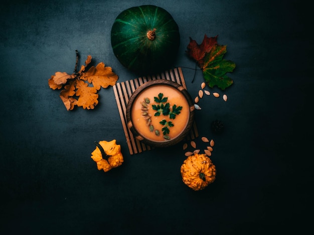 Wooden bowl of traditional pumpkin soup on gray table decorated with seeds parsley colorful foliage decorative pumpkin