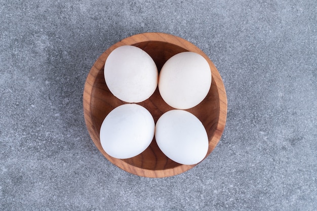 Wooden bowl of uncooked fresh eggs on stone.