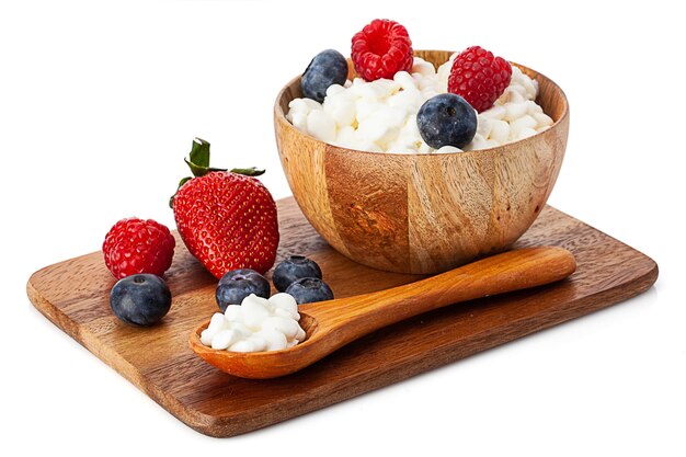 Wooden bowl with cottage cheese and berries standing on wooden board. isolated on white background