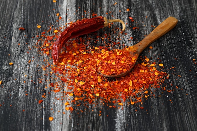 Wooden bowl with crushed chili pepper and fresh red chili pepper on old table Selective focus