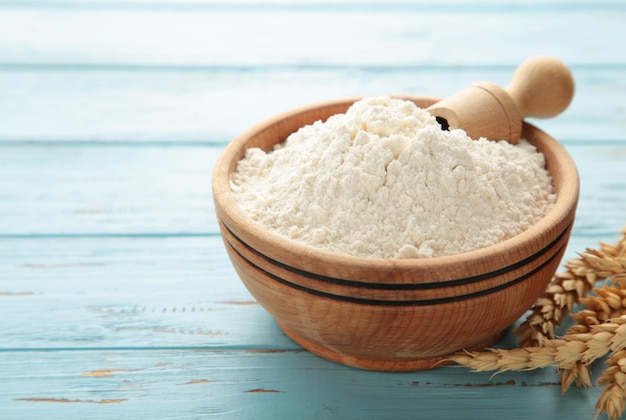 Wooden bowl with flour and flour spoon Rice or wheat flour on blue wooden background top view