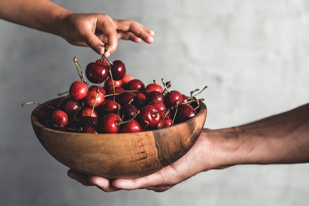 Wooden bowl with fresh juicy berries. Cherries in hands. Organic eco product, farm. Non GMO