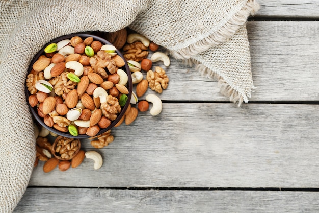 Wooden bowl with nuts on a wooden background, near a bag from burlap.