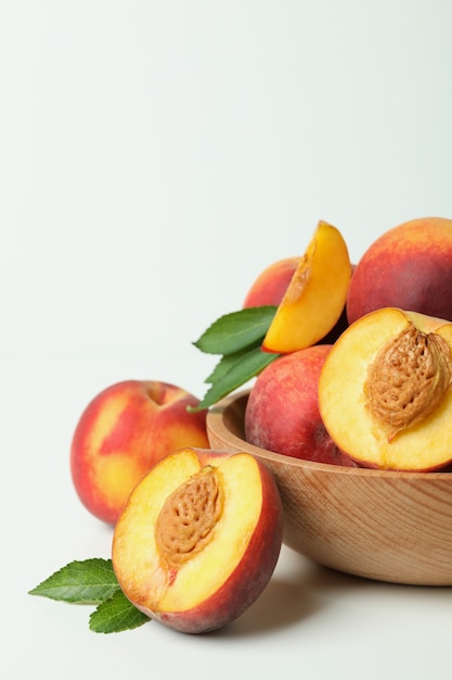 Wooden bowl with peach fruits on white table