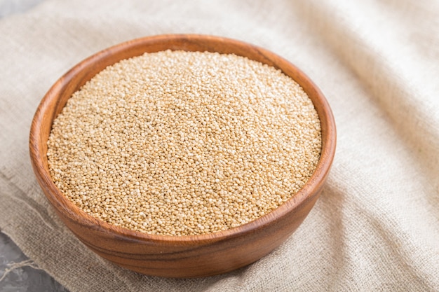 Wooden bowl with raw white quinoa seeds and wooden spoon on a gray concrete