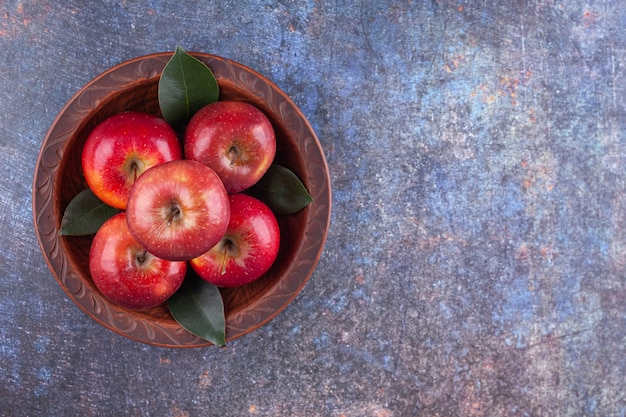 Wooden bowl with shiny red apples on stone background. 