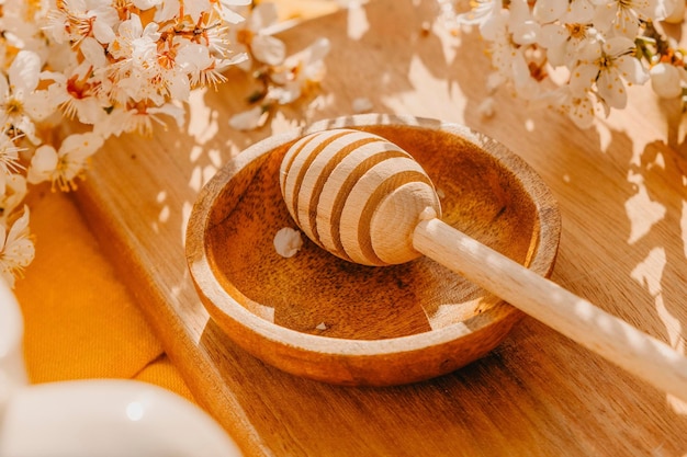 A wooden bowl with a wooden spoon of honey on a table surrounded by flowers