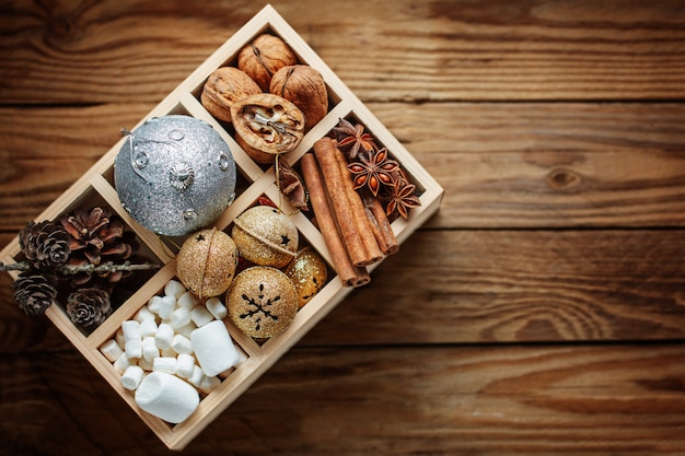 Wooden box filled with Christmas decorations, ball, jingle bells, nuts, cones, cinnamon, marshmallow