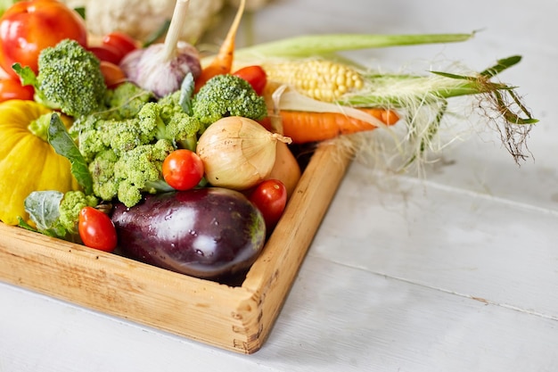 Wooden box with different fresh farm vegetables on the white background