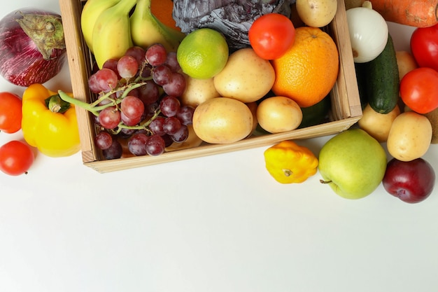 Wooden box with different vegetables and fruits on white table