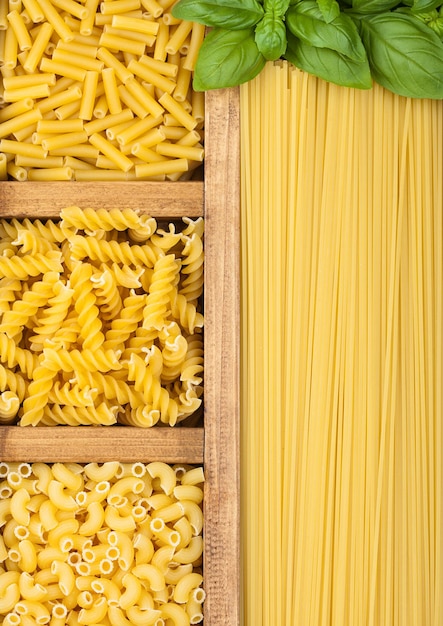 Wooden box with spaghetti and fusilli and macaroni with maccheroni and fresh basil Top view