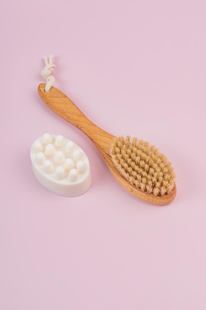 Wooden brush with natural bristle for dry massage preventing cellulite nad massagin soap bar on pink background Home SPA minimalism