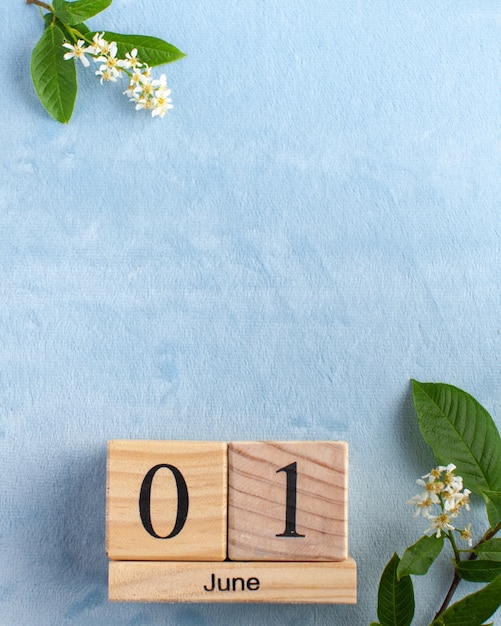 Wooden calendar June 1 on a blue surface with white flowers